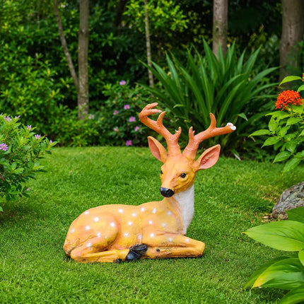 Decorative sitting deer garden statue with antlers placed in a lush green outdoor garden